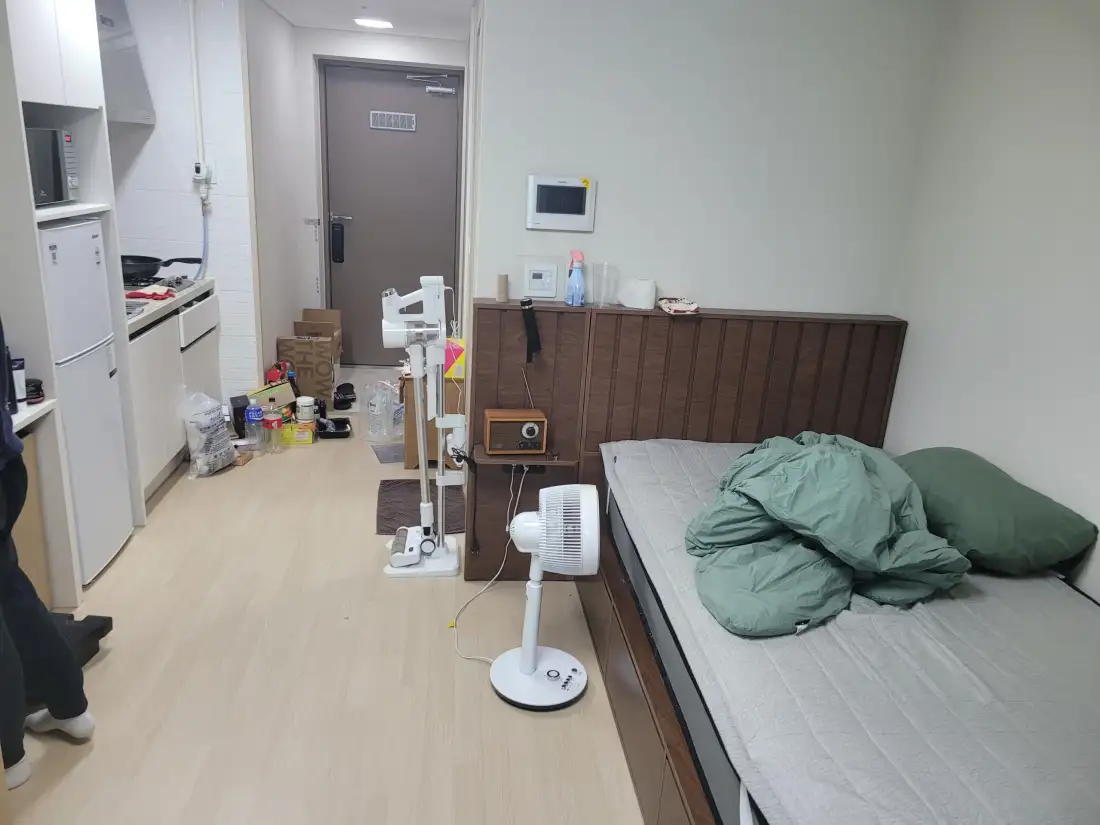 침대와 선풍기, 생활용품이 놓인 원룸 내부 전경